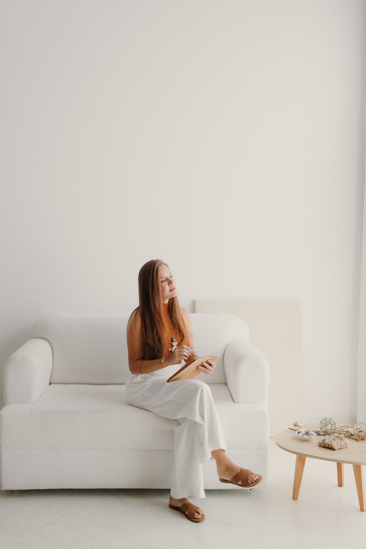 Bruna Veiga, especialista em Feng Shui, sentada em um sofá branco com um tablet
